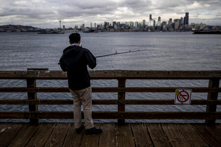 A man stands on a pier while fishing.