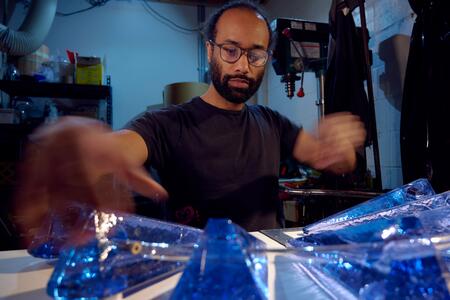 An artist wearing glasses examines blue triangular glass structures